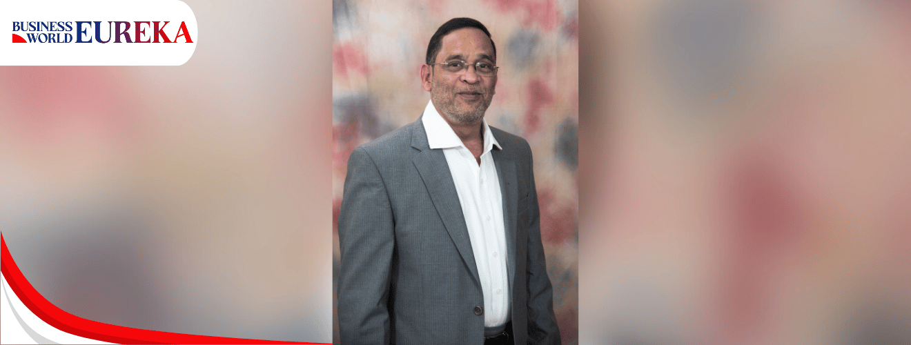 Girish Tilak in a grey suit posing for a formal photograph with a soft multicolor background.