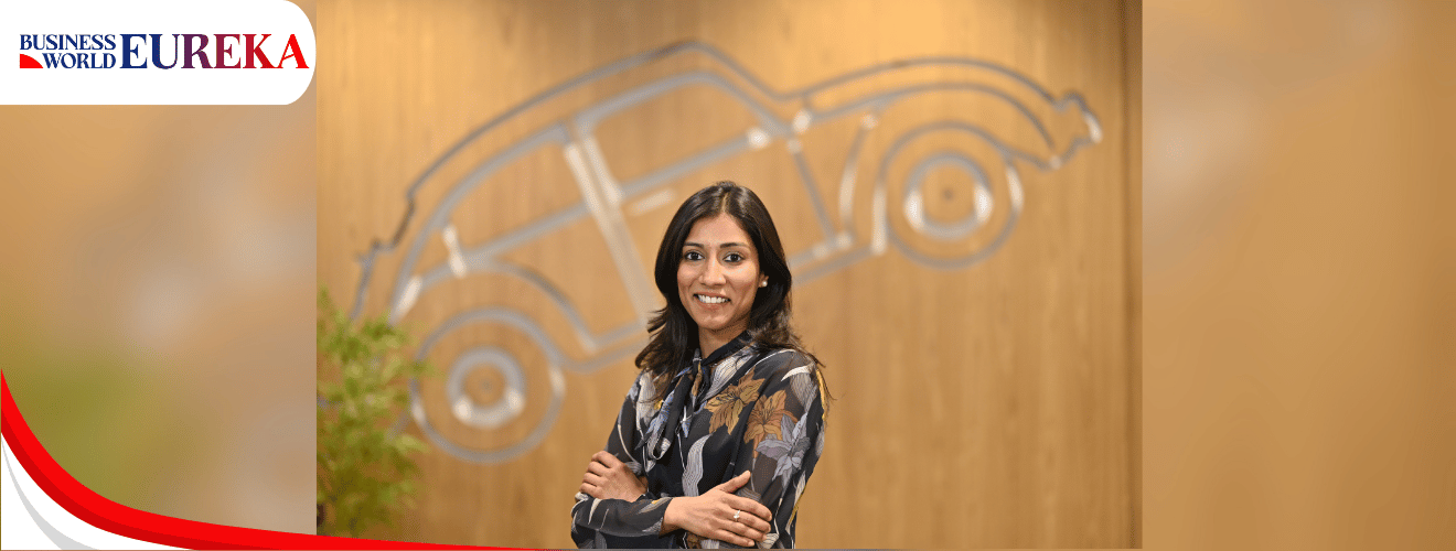 Nehal Gupta standing confidently in front of a wooden wall with a car outline, wearing a floral blouse.